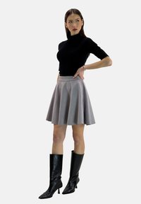 Schwarzes kurzärmeliges Oberteil kombiniert mit einem grauen ausgestellten Rock, kniehohe schwarze Stiefel aus Leder mit spitz zulaufender Zehe. Glatte Texturen und klare Linien.