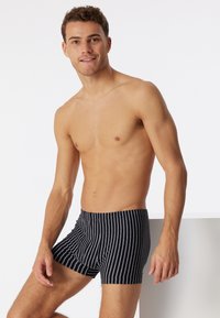 Costumi da bagno a righe bianche e nere con una vestibilità aderente, realizzati in un tessuto morbido. Presentano una vita classica e una lunghezza della gamba corta.
