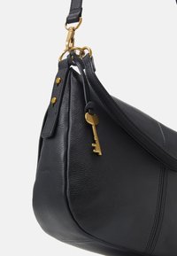 Sac à main en cuir noir avec une forme arrondie, mettant en avant un accent en forme de clé dorée, des accessoires dorés et des détails de couture contrastés.
