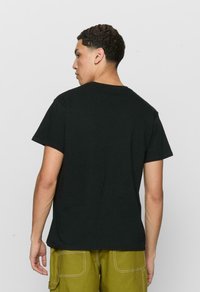 Sort bomulds T-shirt med korte ærmer, rund hals og lige kant. Bæret med olivengrønne bukser med synlige sømme og lommer.