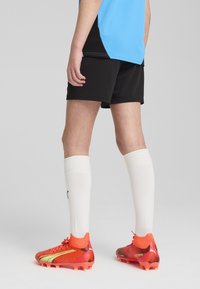 Ryškiai oranžiniai ir raudoni futbolo batai su geltonomis detalėmis, juodi šortai ir baltos iki kelių kojinės. Mėlynas sportinis marškinėliai su juodomis detalėmis.