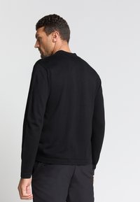 Zwarte gebreide trui met een ronde hals, lange mouwen en een strakke pasvorm. De textuur lijkt glad en licht van gewicht.