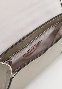 Beżowe wnętrze torebki z gładką fakturą, kieszenią na zamek i etykietą marki. Podszewka satynowa o delikatnym połysku.