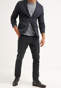 Blazer blu navy slim fit, con un bottone e tasca; camicia grigia texturizzata; pantaloni scuri slim fit; scarpe in pelle nera.