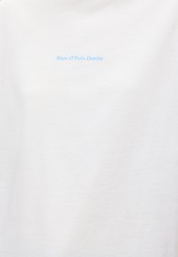 Λευκό ύφασμα με μικρό ανοιχτό μπλε κείμενο "Marc O’Polo Denim" τοποθετημένο στο κέντρο κοντά στο πάνω μέρος.