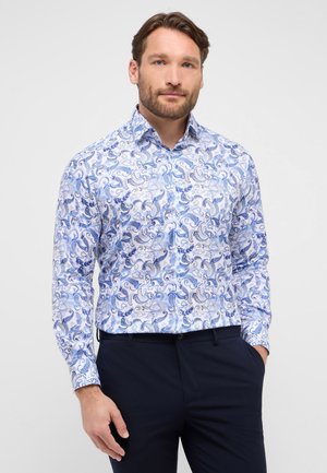 Witte shirt met blauw paisleypatroon, lange mouwen en button-down kraag, gecombineerd met donkere broeken. Heeft een gladde stoftextuur.