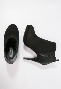 Botín de tacón alto negro con parte superior de ante, detalles grabados en cocodrilo y un elegante tacón de aguja. Presenta una puntera redondeada y paneles elásticos.