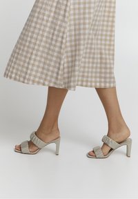 Korkokengät vaaleanharmaana, joissa on poimutetut hihnat ja avoin varvasmuotoilu. Korko on keskipituinen ja siinä on sileä pinta.