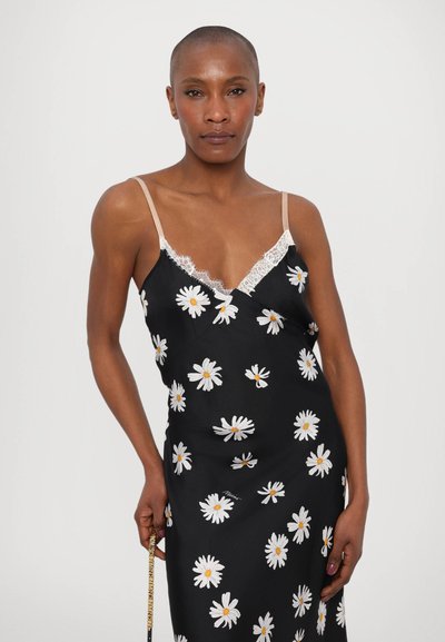 Robe noire sans manches avec imprimés de marguerites blanches, dentelle le long du décolleté et fines bretelles nude. Tissu doux avec une coupe drapée.