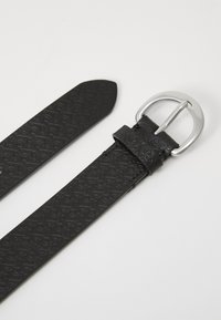 Ceinture en cuir noir avec un motif embélé et une boucle en métal argenté. La sangle est plate et légèrement effilée à l'extrémité.