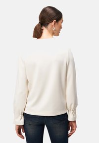 Ivoor kleurige pullover sweatshirt met lange mouwen, gathered cuffs en een ronde halslijn. Glad stoffen textuur en een ontspannen pasvorm, gecombineerd met donkere spijkerbroeken.