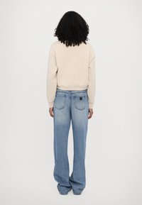 Felpa beige con orlo a costine, abbinata a jeans di denim azzurri a gamba larga con tasche posteriori e finitura distress.