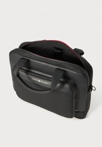 Black laptop bag with dual handles, zippered closure, internal compartments, and red accent lining; features "TOMMY HILFIGER" logo on front.