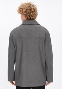 Cappotto grigio di lana con colletto a punte, maniche lunghe e taglio dritto. Presenta linee pulite e nessun sistema di chiusura visibile. Vista posteriore mostrata.