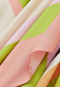 Tissu coloré présentant des motifs géométriques audacieux dans des nuances de rose, de vert et d'orange, avec une texture lisse et tissée.