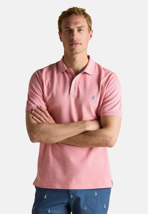 Helles rosa Polohemd mit Kragen, kurzen Ärmeln und einem kleinen blauen Logo auf der Brust. Trägt dazu kurze blaue Hosen mit einem Muster aus kleinen Leuchtturmdesigns.