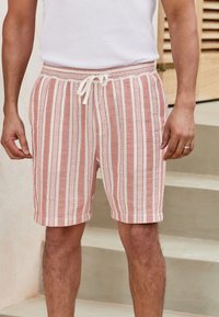 Pantalones cortos a rayas en rosa claro y blanco, con una cinturilla elástica y cordón. Hechos de tela texturizada con un ajuste holgado.