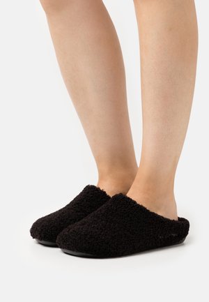 Svarta fluffiga tofflor av mjukt tyg. Stängd tå-design med mjuk, plyschliknande yta och gummisula för bra fäste. Bekväma vardagsskor.