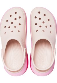 Zuecos de color rosa claro con una suela de rosa más oscuro, que cuentan con múltiples orificios de ventilación, un borde elevado y una correa en el talón para un ajuste seguro.