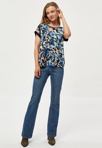 Modrý a béžový top s krátkým rukávem v kamuflážovém vzoru, s černým výstřihem, v kombinaci s modrými zvonovými džínami a olivově zelenými kotníkovými botami.