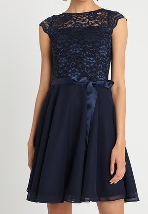 Sukienka bez rękawów w kolorze granatowym, z koronkowym gorsetem, przezroczystym dekoltem, satynową wstążką w talii wiązaną na kokardę oraz zwiewną spódnicą sięgającą powyżej kolan.