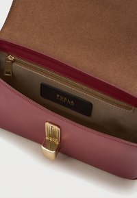 Δομημένη τσάντα χεριού από μπορντό δέρμα, με χρυσές λεπτομέρειες και υφή επιφάνειας. Ο εσωτερικός χώρος περιλαμβάνει μια τσέπη με φερμουάρ και μπεζ επένδυση.