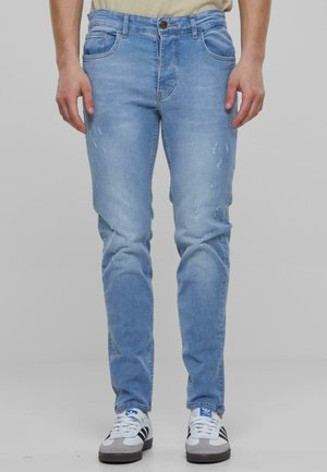 Valkoiset ja harmaat tennarit yhdistettynä vaaleansinisiin farkkuihin, joissa on slim fit -leikkaus, haalistuneita yksityiskohtia ja kevyitä kulumia.