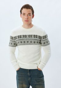 Weißer gestrickter Pullover mit einem grauen geometrischen Muster über der Brust und den Ärmeln. Das Design beinhaltet Schneeflocken-Motive und gerippte Bündchen.