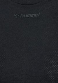Schwarzes Sportshirt aus glattem Stoff, mit Rundhalsausschnitt und eingestanztem Branding. Die Textur zeigt auf einer Seite ein kleines Punktmuster.
