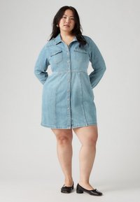 Δημινένιο φόρεμα σε ανοιχτό μπλε, με κουμπιά μπροστά, μακριά μανίκια, τσέπες στο στήθος και εφαρμοστή μέση με φουσκωτό κάτω μέρος.