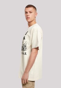 Light beige oversized t-shirt featuring a black graphic print with waves and Japanese text. Short sleeves and a relaxed fit.