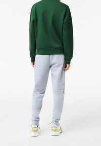 Sudadera verde con puños y bajo acanalados, combinada con pantalones jogger gris claros. Presenta un ajuste relajado, tejido suave y cinturilla elástica.