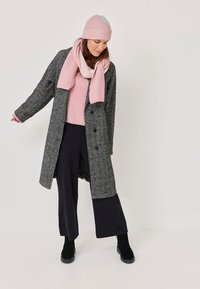 Szary, teksturowany płaszcz, różowy prążkowany szalik i czapka, jasnoróżowy sweter, czarne szerokie spodnie i botki za kostkę. Prosty, funkcjonalny styl.