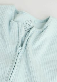 Lyseblå babyheldragt med ribbet tekstur, udstyret med lynlås foran og rund halsudskæring. Vaskeanvisning synlig indeni tøjet.