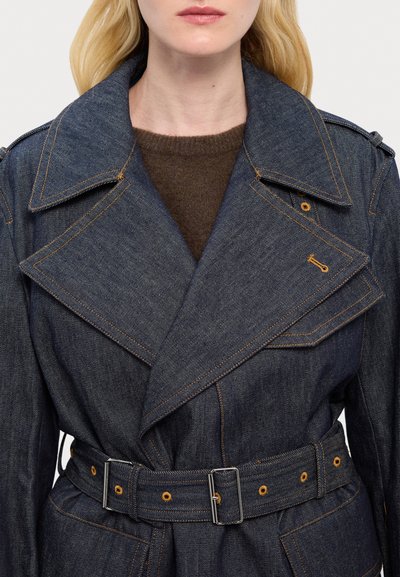 Manteau en denim avec un large col cranté, un design à double boutonnage et une taille ceinturée. Présente des coutures orange et des accents en métal.