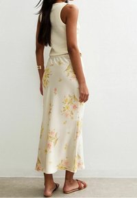 Kvítkovaná midi sukně v světlé krémové barvě s růžovými a žlutými květinovými vzory, doplněná žebrovaným, bez rukávů topem a hnědými pohodlnými sandály.