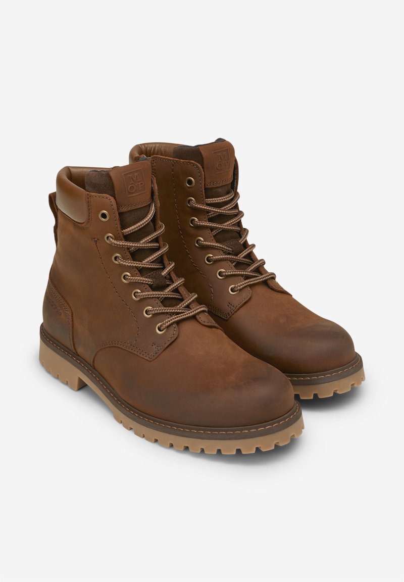 Botas de cuero marrón hasta el tobillo con puntera redonda, cuello acolchado y ojetes de metal. Suela de goma marrón claro con un dibujo profundo para mayor tracción.