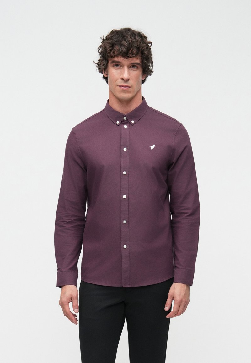 Hosszú ujjú, bordó gombos ing, pamut anyagból. Klasszikus gallérral, fehér gombokkal és egy kis fehér logóval a mellkasán.