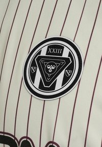 Hvid trøje med tynde burgunder striber, prydet med et cirkulært sort-hvidt emblem, der viser en trekant, et kranievejr og teksten "XXIII."