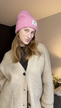 Cardigan côtelé beige clair avec des boutons sur le devant et des poches, associé à un bonnet rose vif avec un patch logo blanc.