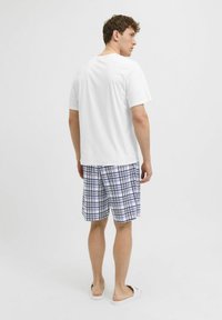 White short-sleeve t-shirt, blue and white plaid shorts, and white slides, viewed from behind against a plain background.