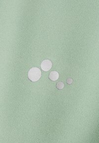 Ljusgrön tyg med en strukturerad yta som har ett mönster av fem överlappande silvercirklar i varierande storlekar.