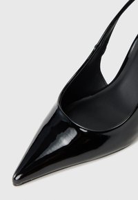 Sorte lakkleder høyhælte sko med spiss tå og åpne sider, med en glatt, blank overflate og en elegant silhuett.