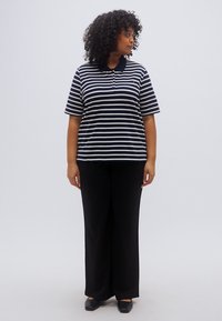 Μπλούζα πόλο με κοντά μανίκια σε ασπρόμαυρες ρίγες, γιακάς, συνδυασμένη με μαύρο παντελόνι φαρδιάς γραμμής και επίπεδα παπούτσια. Απλός, άνετος σχεδιασμός.