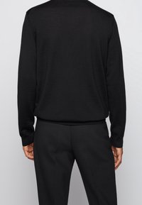 Černý svetr s jemnou texturou, s kulatým výstřihem a dlouhými rukávy, spárovaný s černými kalhotami, obojí v jednoduchém, klasickém designu.