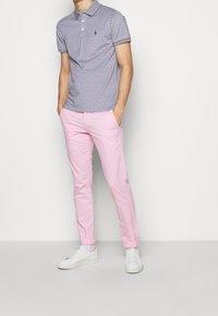 Randig polo-shirt i marinblått och vitt, parat med ljusrosa chinos. Vita sneakers. Modellen står med händerna i fickorna.