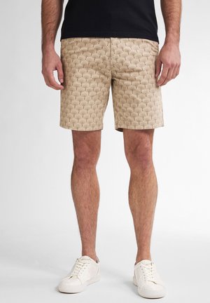 Beige shorts with a repeating palm leaf pattern, made of lightweight fabric. Paired with white sneakers, standing against a light background.