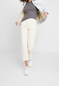 Krämfärgade kordbyxor med rak passform, i kombination med en grårandig skjorta och en ljusblå denimjacka. Vita sneakers fulländar looken.