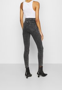 Jeans ajustados de tiro alto en denim negro desgastado con una textura sutil, que presentan bolsillos traseros y un dobladillo desgastado, combinados con botas de tacón negras.