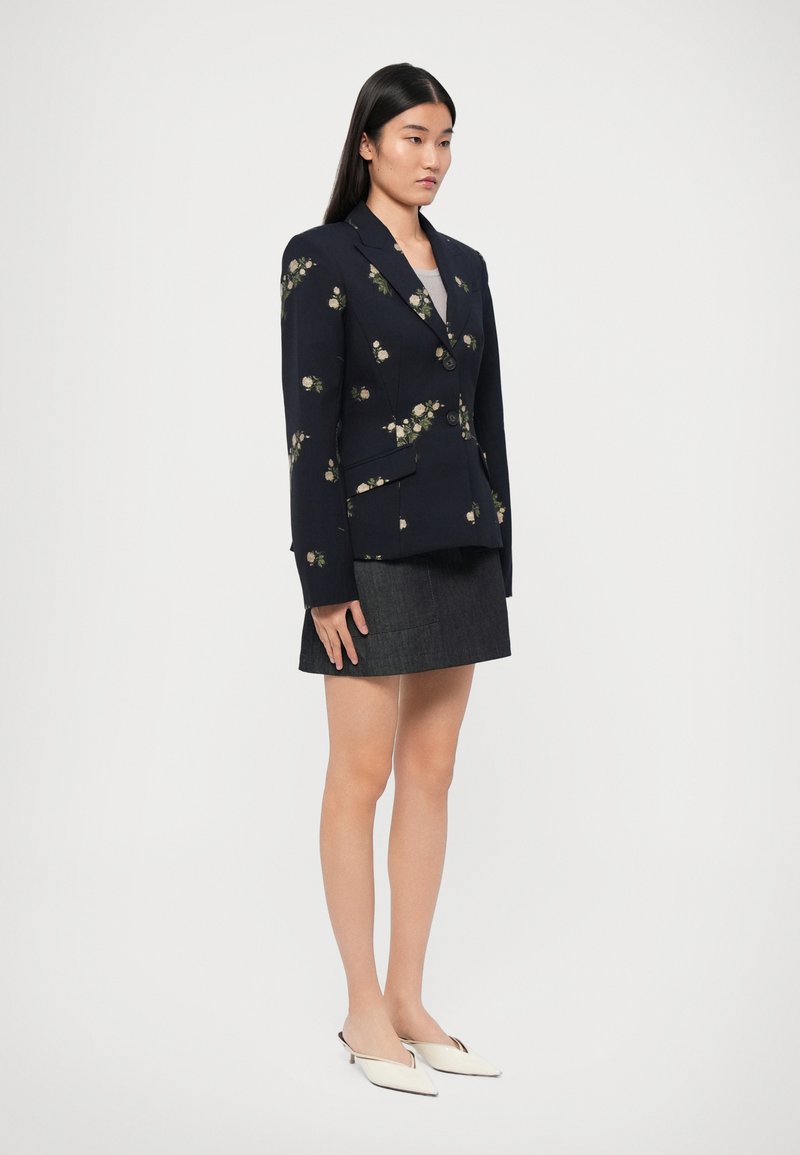Navy blazer met bloemenborduursel, voorzien van twee knopen en zakken, gecombineerd met een donkerdenimrok en witte, puntschoen mules.